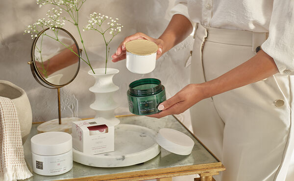 Person refilling a The Ritual of Jing body cream jar, plus a The Ritual of Sakura body cream refill on a dressing table.